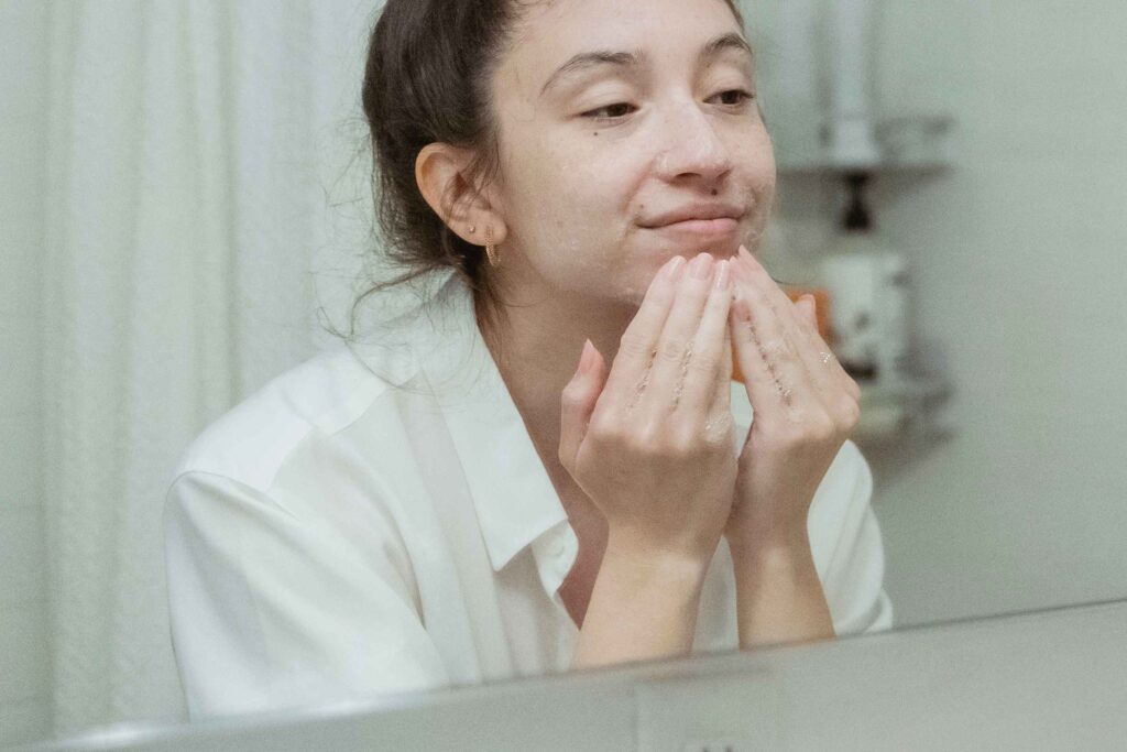 Teen girl following an oily skin skincare routine in the bathroom mirror