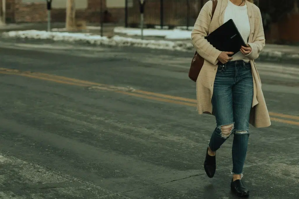 Back to School Outfits for Women: 5 Styles That Work All Day 4 Woman wearing layered back to school outfit — white tee, jeans, cardigan tied at waist, structured backpack